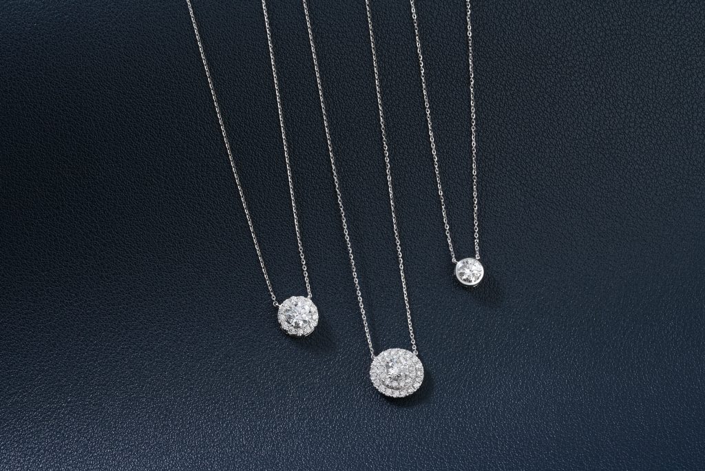 Three luxurious diamond necklaces elegantly displayed on a textured dark blue background.